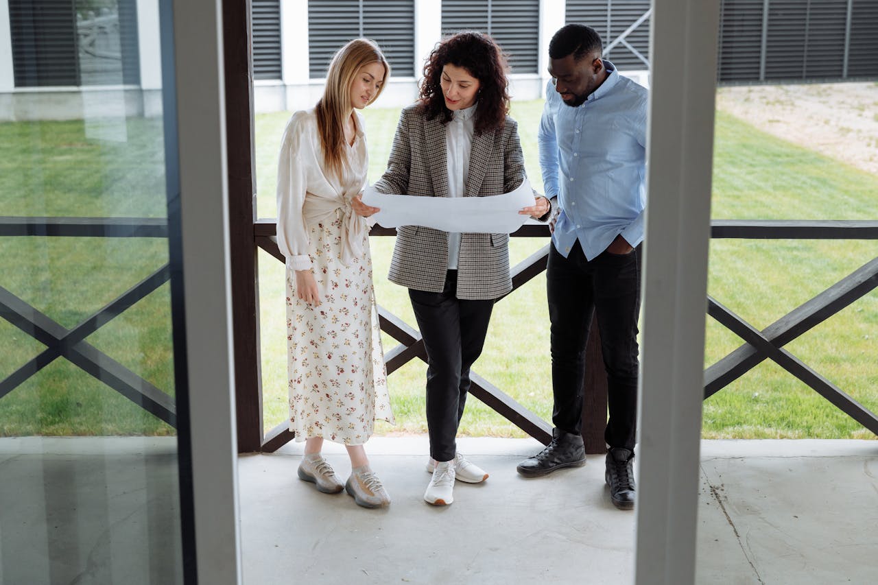 about-03 A realtor with clients examining a floor plan outside a modern property.