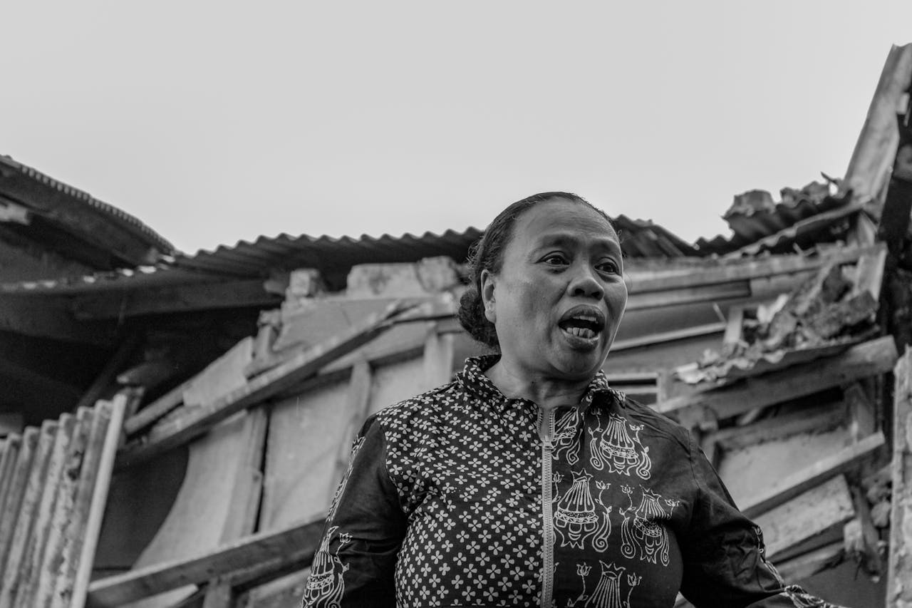 about-04 Black and white portrait of a woman standing in front of a damaged house, Cianjur, Indonesia.