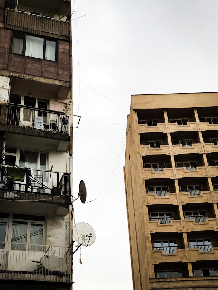 about-02 Two adjacent residential buildings with balconies and satellite dishes in an urban setting.