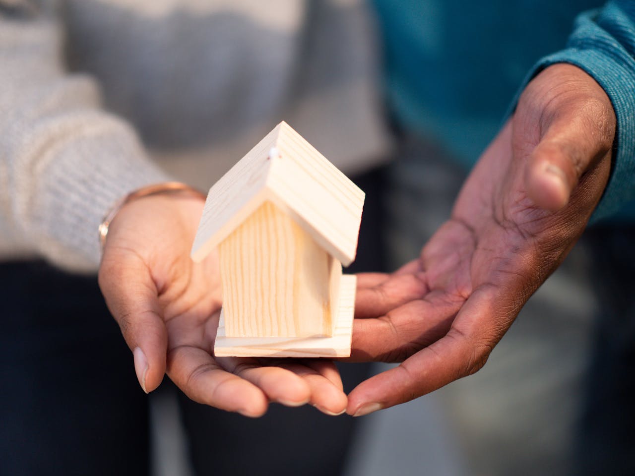 why-choose-us-02 Hands holding a small wooden house model, symbolizing new home ownership and real estate transactions.